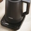 A close-up shot of a black electric kettle on its charging base, with its control panel visible. Podgląd zdjęcia produktu