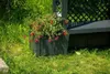 A garden bench with planters and a trellis is set in a grassy area with lush green foliage. Produktbild-Vorschau