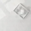 A white tray with decorative items on a textured white surface, with light casting shadows. Produktbild-Vorschau