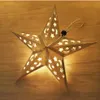 A lit paper star lantern with cutouts of stars and moons rests on a wooden surface. Podgląd zdjęcia produktu