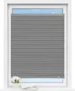 A grey pleated blind is shown covering most of a window, with a small portion of the sky visible above. A small bouquet of white flowers in a pot and an open book are on the windowsill below. Produktbild-Vorschau
