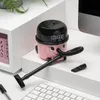 A small pink and black desk vacuum cleaner shaped like a cartoon character is placed on a white surface next to a keyboard and a computer monitor. Produktbild-Vorschau