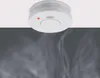 A smoke detector is mounted on a white ceiling, with smoke rising from below. Produktbild-Vorschau