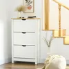 A white shoe cabinet with a natural wood top is placed in a hallway next to a wooden staircase. Decorative items like a vase with dried grass, sunglasses, and a hat are on top of the cabinet. A pouf with a blanket is on the floor next to it. Produktbild-Vorschau