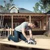A man is kneeling on a wooden deck, using a circular saw to cut a piece of plywood. The house is under construction in the background. Anteprima dell’immagine prodotto