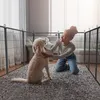 A young woman is kneeling inside a dog playpen, petting her dog. Náhled obrázku produktu