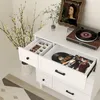A white dresser with opened drawers, showcasing a jewelry organizer and vinyl records. Produktbild-Vorschau