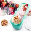 A teal ice cream container filled with pink ice cream, topped with strawberries and nuts, with a waffle and berries in the background. Produktbild-Vorschau