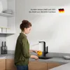 A woman is washing a yellow tomato under a black kitchen faucet. Produktbild-Vorschau