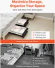 Two under-bed storage containers filled with folded clothes and bedding are shown next to a bed. The image also shows a cluttered bedroom floor with clothes scattered on the bed and a nightstand. Anteprima dell’immagine prodotto