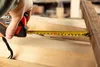 A hand is holding a tape measure and measuring a wooden surface. Produktbild-Vorschau