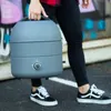 A person is carrying a portable grill outdoors, with graffiti art in the background. Produktbild-Vorschau