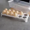 A white egg holder with 10 eggs on a gray surface, with a clear plastic container in the background. Podgląd zdjęcia produktu