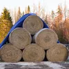 A stack of hay bales covered by a blue tarp, with trees in the background. Produktbild-Vorschau