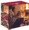 A woman sits by a fireplace, holding a mug, with an advent calendar in the foreground. Produktbild-Vorschau