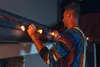 A man is hanging string lights on the gutter of a house at night. Podgląd zdjęcia produktu