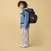 A young boy wearing a backpack and casual clothes, standing against a plain background. Anteprima dell’immagine prodotto