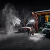 A man is using a snow blower at night in the snow, with snow spraying from the machine. Produktbild-Vorschau