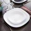 A table setting with white square plates and a bowl, a wine glass, and cutlery. Anteprima dell’immagine prodotto