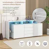 A white sideboard with blue LED lighting, decorated with vases and a clock, set in a room with a floor lamp and a plant. Voir les images du produit