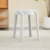 A white stool is placed on a textured rug in a room with a wooden shelf unit and a potted plant in the background. Voir les images du produit