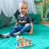 A young boy is sitting on a green mat with a toy pyramid in front of him. Produktbild-Vorschau