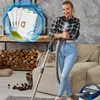 A woman is posing with a vacuum cleaner in a living room setting, with a fireplace and sofa visible. Voir les images du produit