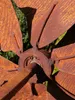 A close-up view of a rusty metal wind spinner with multiple blades, set against a blurred green background. Produktbild-Vorschau