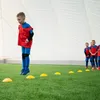 Children in soccer uniforms practicing on a green field indoors. Náhled obrázku produktu