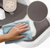 A hand is cleaning a gray surface with a blue cloth, with a close-up of the textured gray material in a circle. Voir les images du produit