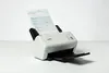 A document scanner is shown on a white surface with a document being fed into it. Voir les images du produit