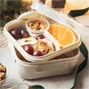 A beige lunchbox filled with snacks like grapes, dried apples, nuts, and an orange slice, with a lid open and resting against the back. Podgląd zdjęcia produktu