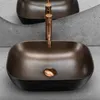 A close-up shot of a modern, oval-shaped vessel sink with a textured black base and a bronze interior. A copper-colored faucet is positioned behind the sink. Anteprima dell’immagine prodotto