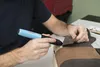 A person is using a cordless hot glue gun to attach a piece of brown fabric to a light-colored object. Produktbild-Vorschau