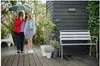 Two people walking under an umbrella on a wooden deck next to a modern house. Anteprima dell’immagine prodotto