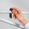 A hand is shown adjusting a black strap attached to a silver metal frame. Produktbild-Vorschau