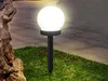 A solar garden light with a white globe sits in the grass next to a stone. Náhľad obrázku produktu