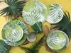 A collection of tableware with a tropical leaf pattern, arranged on a yellow textured surface with decorative green leaves. Náhľad obrázku produktu