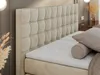 A close-up view of a beige upholstered headboard and mattress topper. Produktbild-Vorschau
