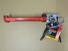 A red caulking gun with a black handle and a product tag attached, lying on a light brown background. Produktbild-Vorschau