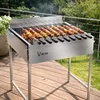 A stainless steel charcoal grill with skewers cooking food outdoors on a wooden deck. Podgląd zdjęcia produktu
