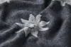A close-up of a dark gray blanket with a white edelweiss flower pattern. Produktbild-Vorschau