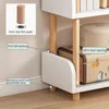 Close-up of the bottom section of a white shelf unit with wooden legs, showing features like anti-slip pads and layer spacing. Produktbild-Vorschau
