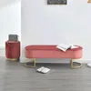 A pink velvet bench and a matching stool are placed on a gray wooden floor in front of a white wall. A handbag is on the stool, and a book is on the bench. A pair of slippers is on the floor in front of the bench. Náhľad obrázku produktu