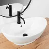 A white oval countertop sink with a black faucet is shown on a wooden surface, with a reflection in a mirror behind it. Náhled obrázku produktu