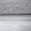 A close-up view of a gray fluffy rug on a light gray wooden floor. Produktbild-Vorschau