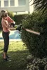 A woman is trimming a bush with an electric hedge trimmer in a garden. Podgląd zdjęcia produktu