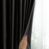 A hand is pulling back a dark curtain to reveal a sheer white curtain behind it. Produktbild-Vorschau