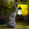 A solar-powered elephant statue holding a lantern in a garden setting. Produktbild-Vorschau