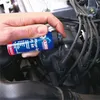 A hand is holding a spray can and applying spray to the spark plug wires of a car engine. Produktbild-Vorschau